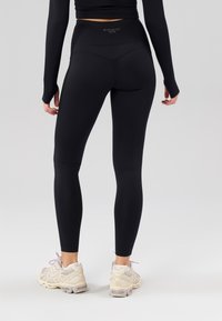 Schwarze, aktive Leggings mit hohem Bund und glatter Textur, kombiniert mit hellfarbenen Sportschuhen mit Schnürdetails.