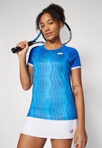 Blue athletic shirt with a textured pattern, short sleeves, and white trim, paired with a white skirt. A tennis racket is held in one hand.