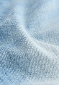 Hele sinine denimkangas pehme tekstuuriga, millel on peened diagonaalsed kudumismustrid. Pind näitab kergeid värvimuutusi.