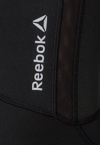 Schwarze Sportleggings mit glatter Textur, grauem Reebok-Logo und Mesh-Einsätzen für Atmungsaktivität entlang der Seitennaht.
