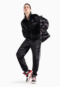 Tuta in velluto nero con giacca con zip, pantaloni abbinati e sneakers rosso/nere con motivi audaci e accenti di logo.