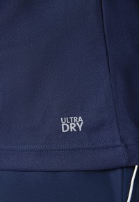 Tessuto blu navy con un motivo texturizzato, caratterizzato da un'etichetta bianca "ULTRA DRY" nell'angolo inferiore, che indica proprietà traspiranti.