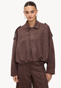 Veste marron en suédine synthétique avec une coupe décontractée, col arrondi et fermeture éclair. Dotée d'épaulettes aux épaules et de manches longues.