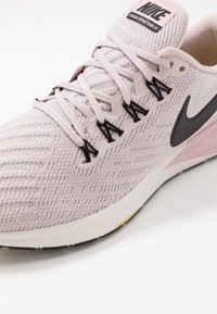 Chaussure de course Nike Zoom Structure 22 rose clair avec tige tricotée, swoosh noir et lacets croisés sur fond blanc.
