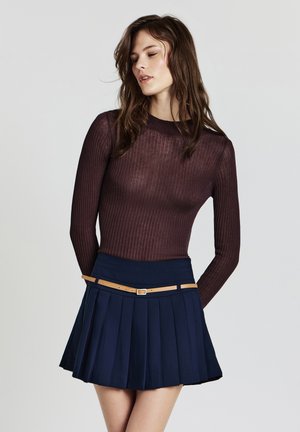Haut à manches longues côtelé marron foncé associé à une jupe plissée bleu marine, avec une ceinture beige accentuée autour de la taille.