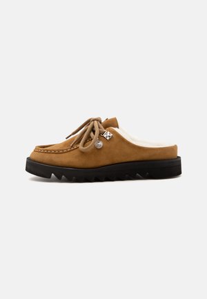 Brown suede slip-on shoe with white fur lining, round laces tied in a bow, metal eyelets, and thick black jagged sole.