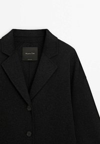 Manteau en laine noir à simple boutonnage avec revers crantés, deux boutons et une étiquette de marque Massimo Dutti visible à l’intérieur du col.