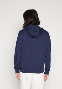 Felpa blu navy con cappuccio regolabile e polsini a costine. Presenta dettagli con logo sulla manica ed è realizzata in un tessuto morbido.
