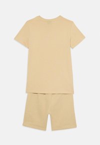 Tvådelad set i ljusbeige bomull, bestående av en t-shirt med kort ärm och matchande shorts. Mjuk textur med en enkel, sammanhängande design.