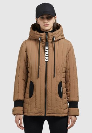 Veste matelassée marron avec capuche, accents noirs, quiltage vertical et fermeture éclair à l'avant. Comprend des poches latérales et un logo en évidence. Tissu texturé.