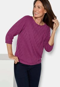 Fuchsia gebreide trui met een textuurpatroon, ronde halslijn en driekwart mouwen, gecombineerd met donkere blauwe jeans.