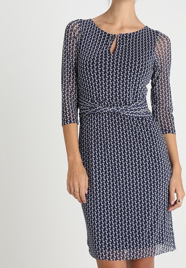 Femme portant une robe bleu marine à motifs, longueur genou, avec manches trois-quarts transparentes et petite goutte d'eau à l'encolure devant.