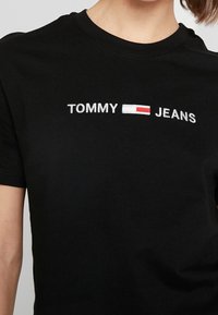 Černé bavlněné tričko s bílým vyšíváním "TOMMY" a "JEANS", mezi textem červený a bílý emblém. Klasický kulatý výstřih.