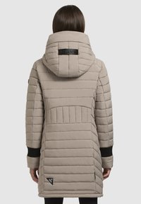 Abrigo acolchado beige con capucha, con costuras horizontales, puños negros y un parche de logo en la parte trasera. Textura suave y diseño de longitud media.