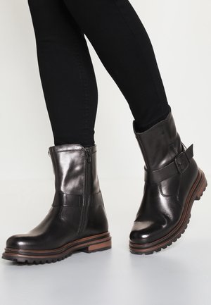 Bottines en cuir noir avec une finition brillante, une fermeture éclair sur le côté et un accent de boucle, avec une semelle robuste et un entrebrosse de couleur marron.