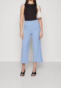 Černý bezrukávový top spárovaný s světle modrými kalhotami širokého střihu, které mají vysoký pas a přední švy. Nosí se s černými sandály na podpatku.