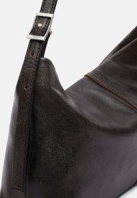 Ciemnobrązowa skórzana torba na ramię z regulowanym paskiem i srebrną kwadratową klamrą, z widoczną teksturą powierzchni i detalami szwów.