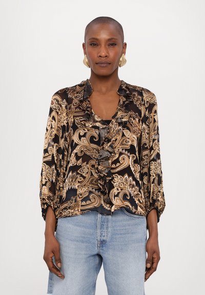 Black blouse with gold paisley pattern, ruffled collar, and three-quarter sleeves. Paired with light blue jeans, featuring a relaxed fit.