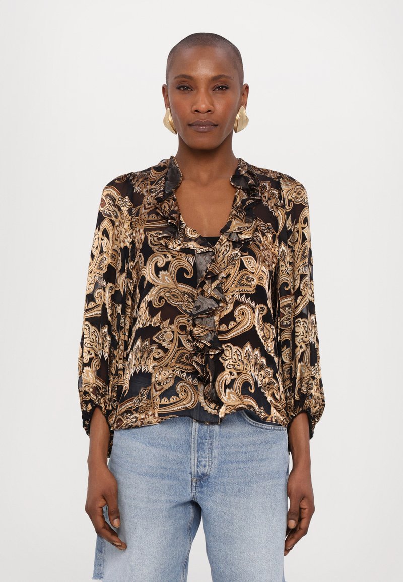 Black blouse with gold paisley pattern, ruffled collar, and three-quarter sleeves. Paired with light blue jeans, featuring a relaxed fit.