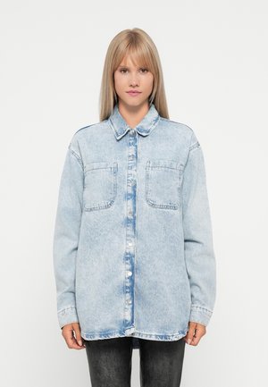 Light blue denim shirt with a button-up front, two chest pockets, long sleeves, and a collar. Distressed texture and soft finish.