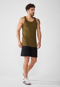 Olivgrünes Ripp-Top kombiniert mit schwarzen Sportshorts und weißen Sneakers, mit einem lässigen Schnitt und minimalistischer Gestaltung.