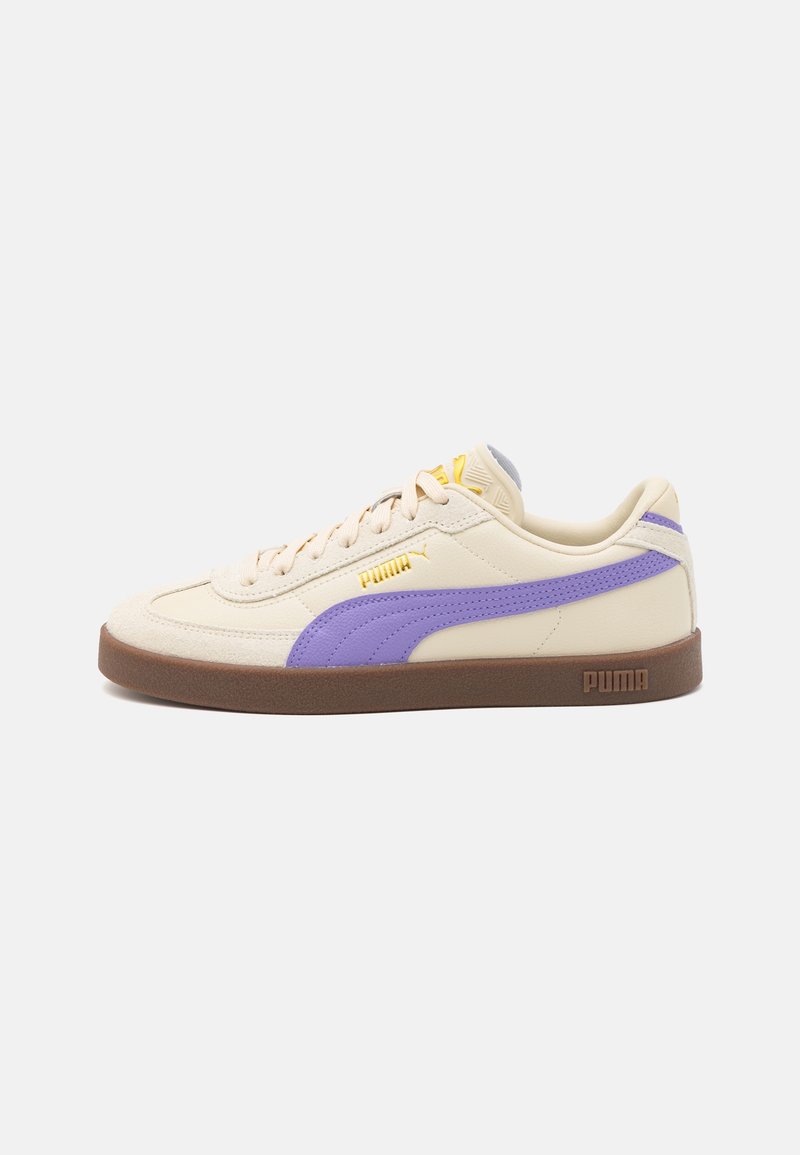 Baskets Puma couleur crème avec une bande violette, logo jaune, semelle marron et lacets sur fond blanc, vue latérale.
