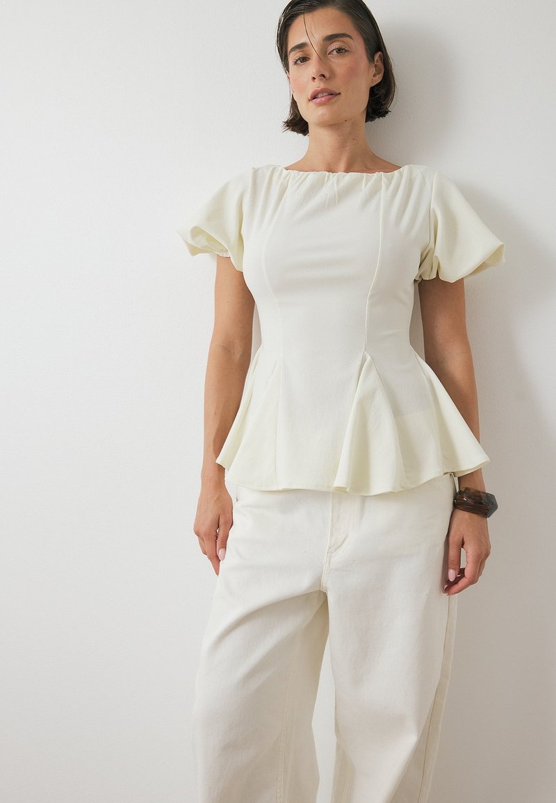 Witte peplumtop met pofmouwen, een gladde textuur en een getailleerde schouderpartij. Gepaard met lichtgekleurde wijde broek. Eenvoudige ontwerpelementen.