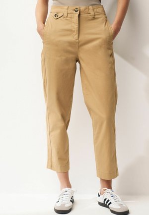 Beige katoenen chinos met een cropped lengte, twee voorzakken, knoopsluiting in de taille en subtiele stiksels aan de zijkanten, gecombineerd met witte sneakers.