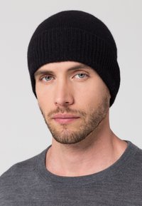 Knit black beanie with a ribbed texture, fitted design, and rounded top. Worn with a gray crew-neck sweater, close-up of face.