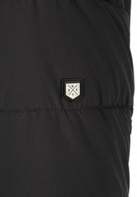 Črn puffer jopič z teksturirano površino. Ima majhen, kvadraten, srebrn logotip v obliki ščita s križanimi elementi.