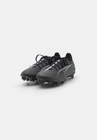 Crampons de football noirs avec une tige texturée, dotés de lignes d'accent en blanc. Conçus avec un profil bas et une semelle en caoutchouc à crampons pour une meilleure traction.