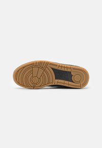 Suela de zapatilla negra con un patrón de goma texturizada, que presenta un diseño circular y un logotipo prominente de Nike en el centro.