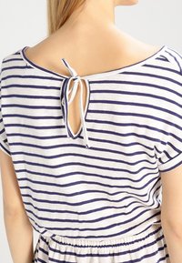 Robe rayée en crème et marine, avec un dos en trou de serrure et une fermeture à nouer, des manches courtes et une taille élastique. Tissu doux.