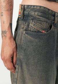 Los pantalones vaqueros de lavado oscuro presentan un corte recto, un ligero desgaste, una pequeña etiqueta de marca en el bolsillo trasero y detalles de costura visibles.
