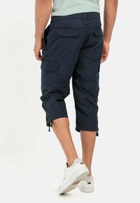 Marine blauwe cargo pants met een relaxte pasvorm, verkorte lengte, trekkoordmanchetten en meerdere zakken. Gemaakt van lichtgewicht stof met een gladde textuur.