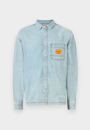 Light blue denim shirt with a button-down collar, long sleeves, a chest pocket featuring an orange label, and white buttons.
