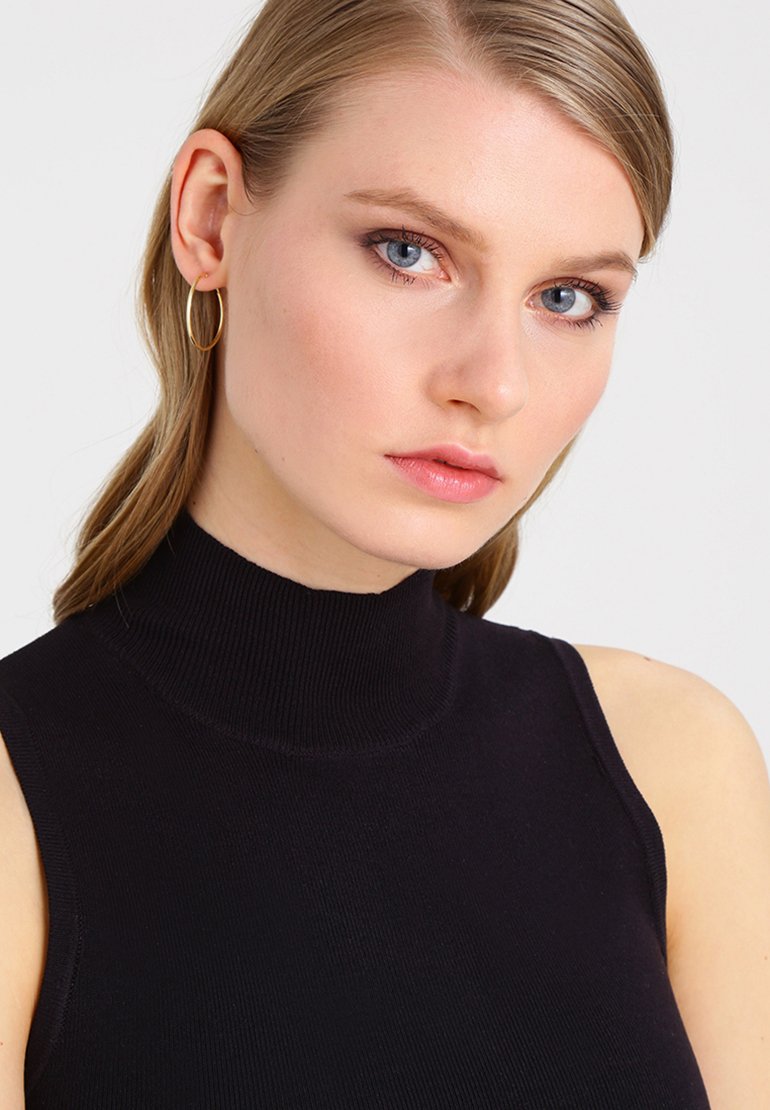 Top negro sin mangas con cuello alto; textura acanalada; tela suave; modelo con cabello largo y aretes de aro delicados.