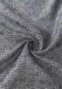 Wovená tkanina v odtieňoch šedej s opakujúcim sa vzorom textu. Mäkká textúra s jemným leskom, vytvárajúca subtílny dimenzionálny efekt.