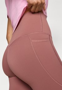 Ροζ κολάν με ψηλή μέση, με απαλή, ελαστική υφή. Διαθέτει αντίθετες ραφές και μικρή τσέπη στο πίσω μέρος.