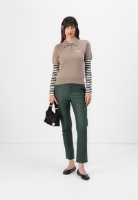 Brun kortärmad polo med ribbat nederkant över en svart-och-vitrandig långärmad skjorta, i kombination med gröna slim-fit byxor och svarta flats.