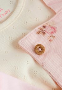 Una tela de corduroy rosa con un diseño floral se superpone a una tela texturada color crema. Un botón de madera redondo con un diseño recortado se destaca de forma prominente.