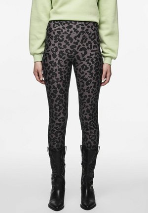 Leggings avec un imprimé léopard foncé portées avec des bottes de cowboy noires et un haut à manches longues vert clair sur un fond blanc.