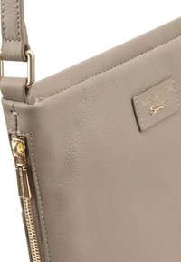 Beige leren schoudertas met gouden rits en rechthoekig logopatch met een klein gouden dierevenement.