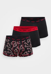 Τρία ζευγάρια boxer briefs με κόκκινη μέση που φέρει το λογότυπο "Diesel". Ένα ζευγάρι έχει σχέδιο με καρδιές από γλειφιτζούρια σε σχήμα καραμέλας, ενώ τα άλλα δύο είναι απλά μαύρα.