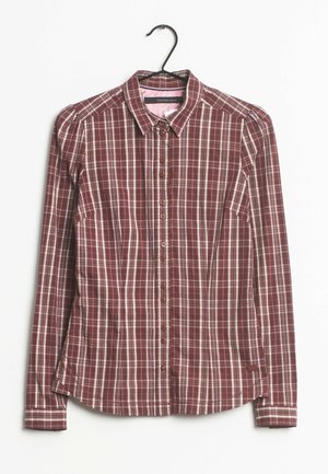 Camisa de mujer de manga larga con botones, patrón de cuadros en rojo y blanco, cuello puntiagudo y silueta ajustada, colgada en percha negra.