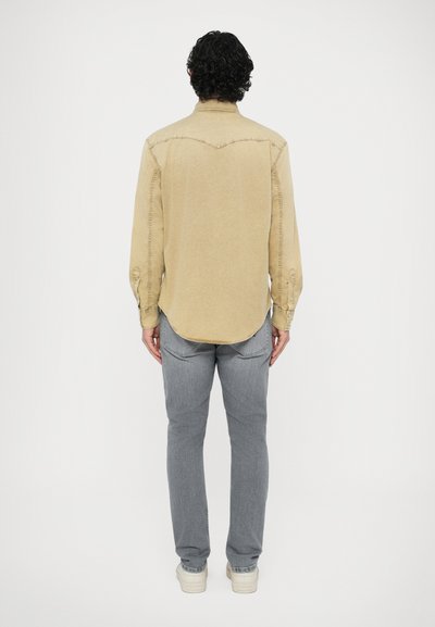 Chemise à manches longues avec ourlet courbé, poignets à boutons et détails cousus. Associée à un jean gris clair et des baskets crème.