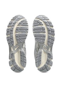 Γκρίζες σόλες αθλητικών παπουτσιών με βαθείς αυλακωτές επιφάνειες, υφασμένα μοτίβα και λευκή μεσαία σόλα. Ενισχυμένες περιοχές για αυξημένη ανθεκτικότητα και πρόσφυση.