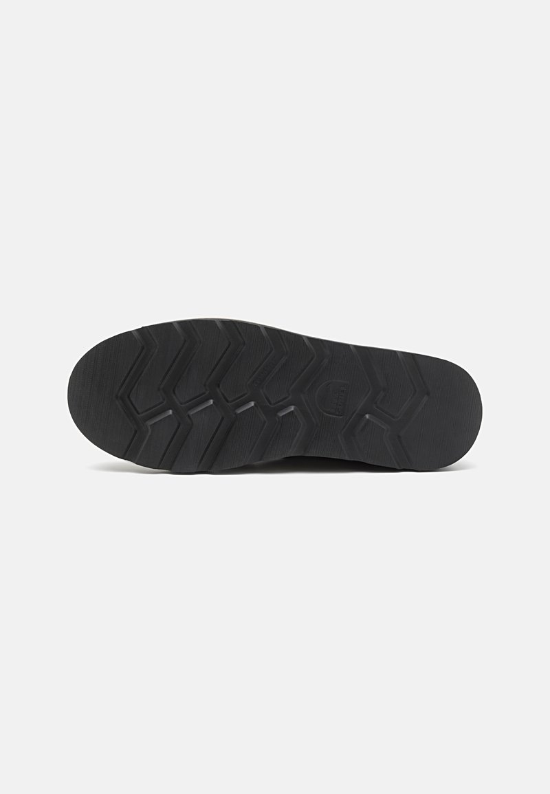 Semelle de chaussure en caoutchouc noir avec un design texturé présentant un motif en zigzag et des rainures pour une meilleure adhérence. Les bords arrondis améliorent la prise.