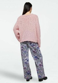 Maglione rosa oversize lavorato a maglia con motivo testurizzato, abbinato a pantaloni grigi con stampa floreale, caratterizzati da una vestibilità ampia e scarpe platform nere.