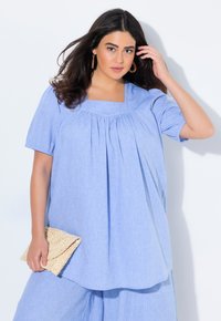 Blusa azzurro chiaro con scollatura quadrata e maniche corte, caratterizzata da delle pieghe per un effetto texturizzato. Abbinata a una borsa a tracolla intrecciata.